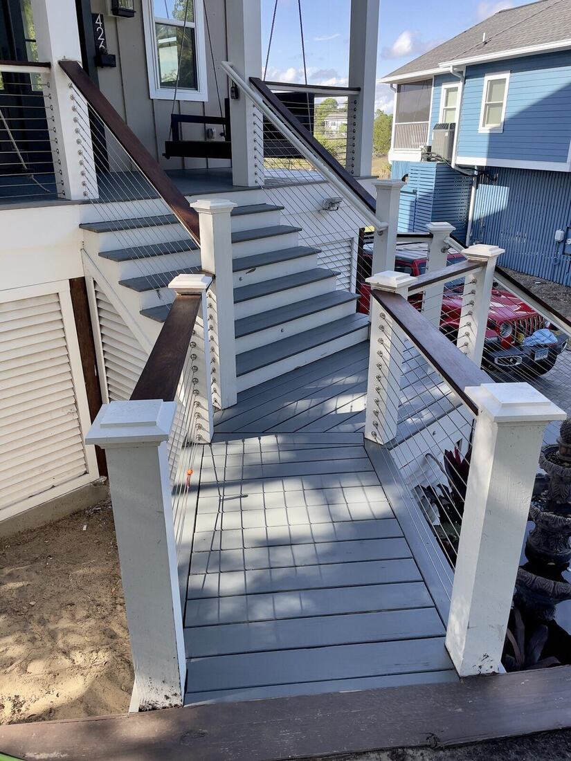 Elevated backyard deck with dark wood cap rail and stainless cable railing, stairs leading down to the driveway.