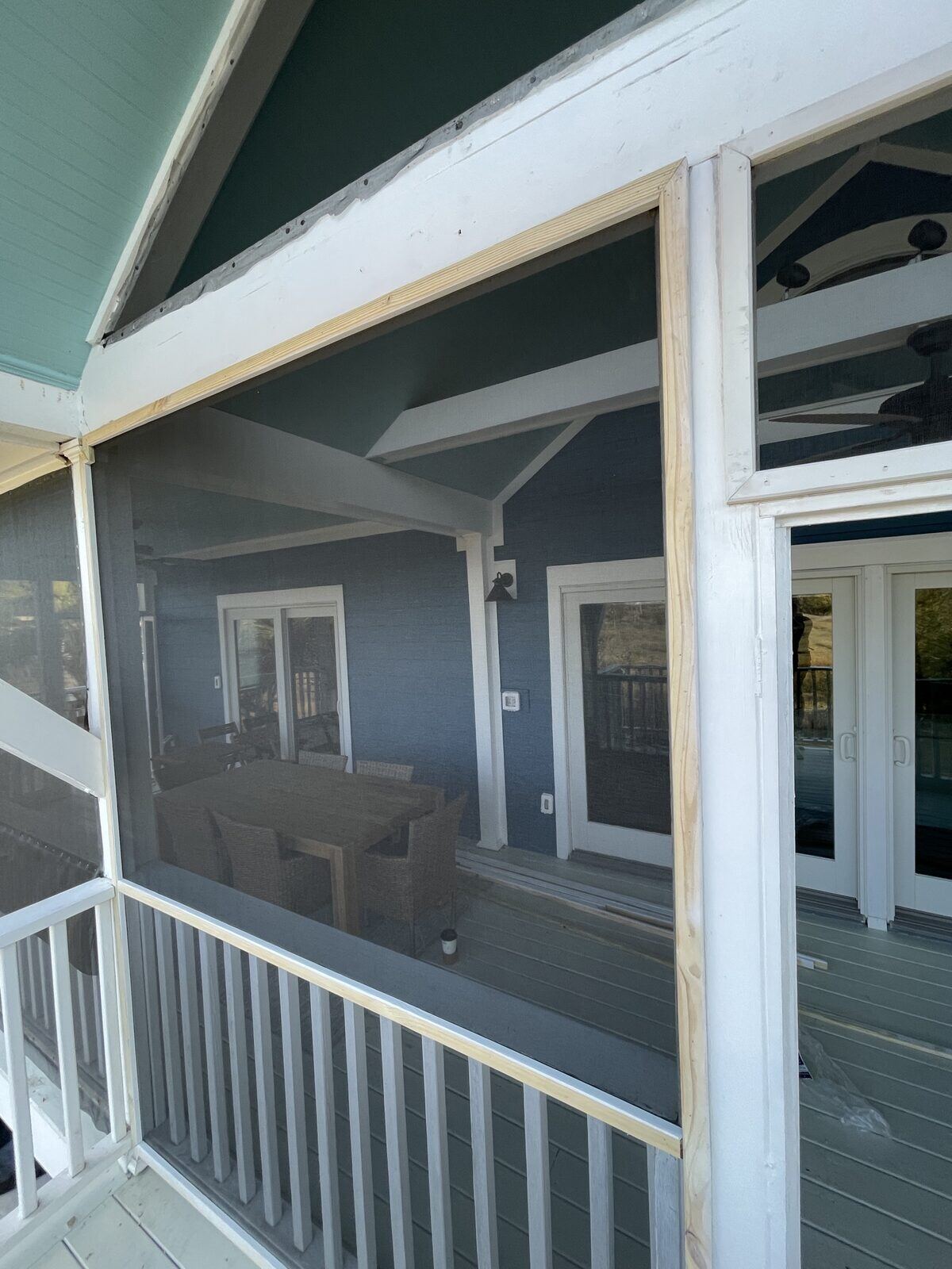 Screened porch with an outdoor dining table and chairs, marsh and tree line visible through the screens.