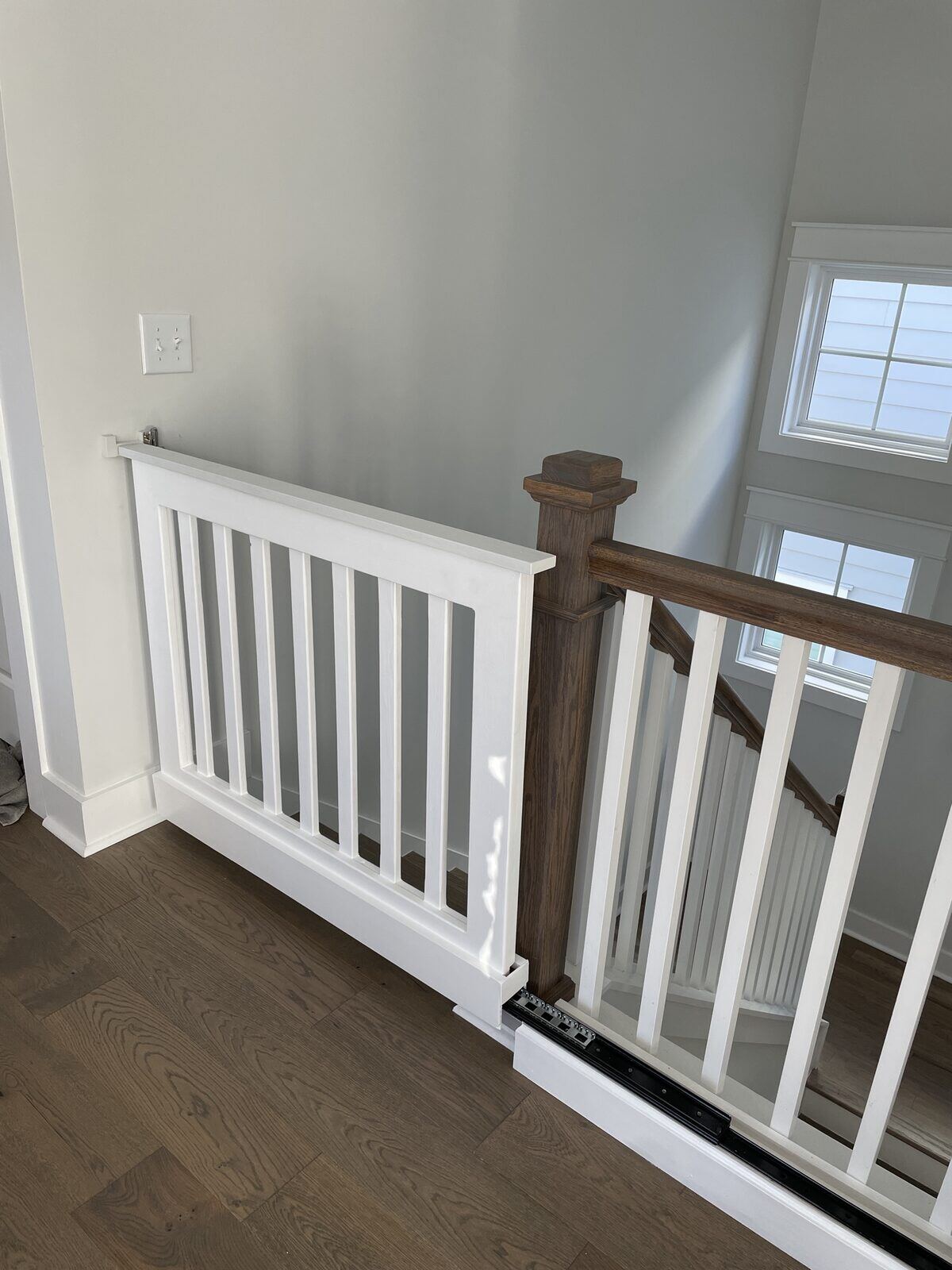 Finished interior stair railing with a dark wood cap rail, dark newel post and white painted balusters.